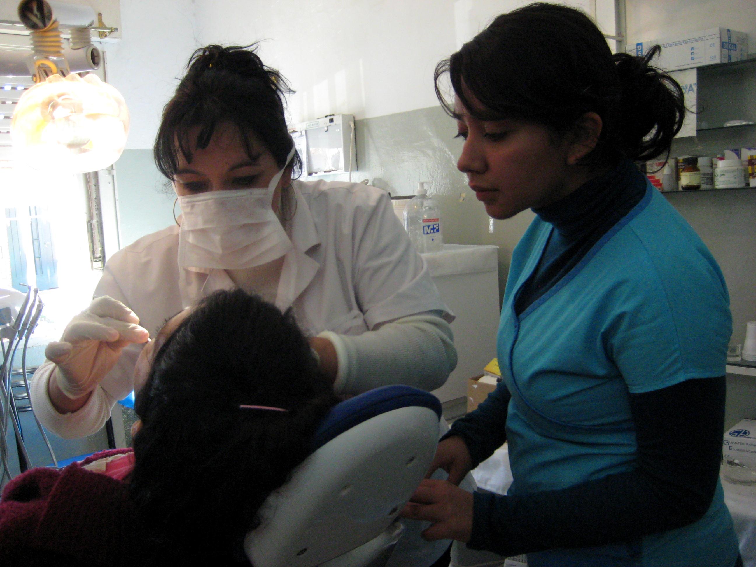 A female Dentistry intern watches a local dentist perform a dental procedure at a clinic in Argentina. A dentist explains a dental procedure to a student doing a Dentistry internship in Argentina.